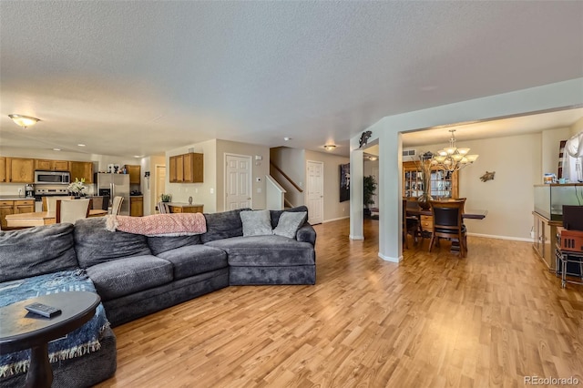 living area featuring light wood-type flooring, a chandelier, stairs, a textured ceiling, and baseboards