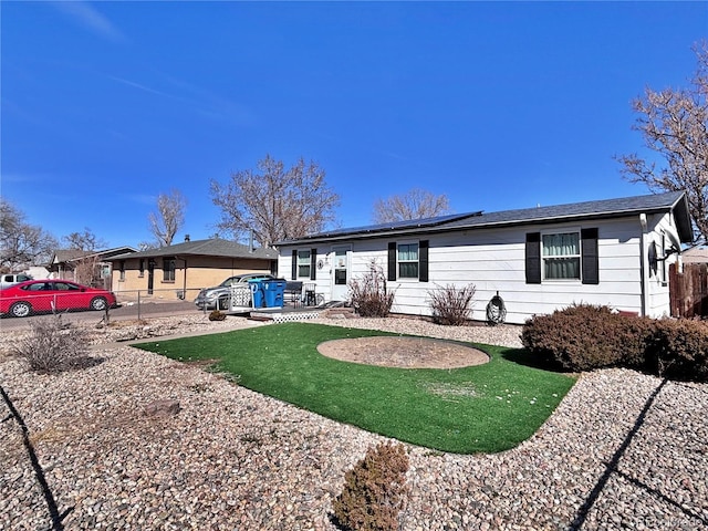 view of front facade with a patio, fence, a front yard, and roof mounted solar panels