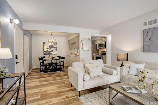 living area featuring light wood-style floors, visible vents, baseboards, and an inviting chandelier