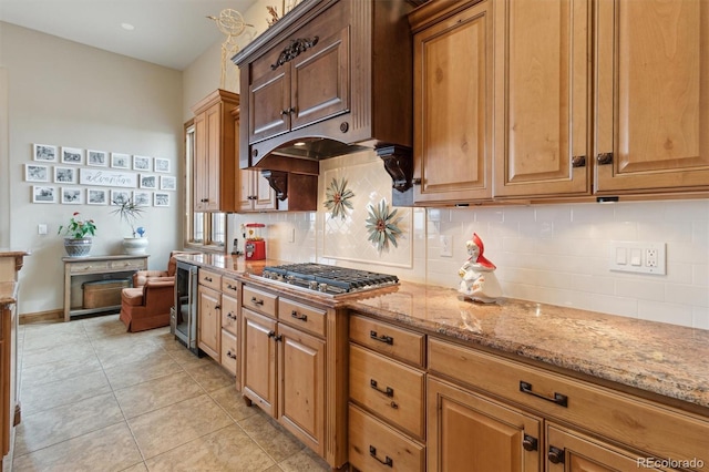 kitchen featuring stainless steel gas cooktop, light stone counters, light tile patterned floors, beverage cooler, and decorative backsplash