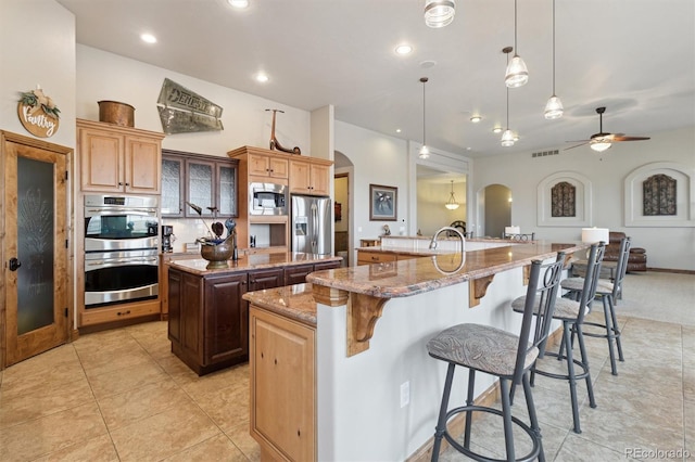 kitchen featuring decorative light fixtures, a kitchen bar, light stone counters, stainless steel appliances, and a spacious island