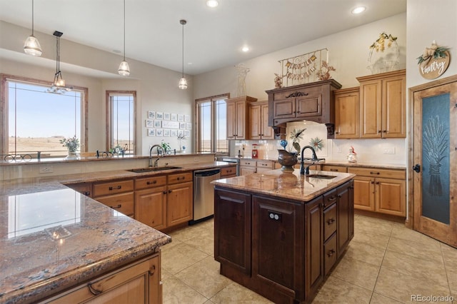 kitchen featuring sink, decorative light fixtures, stainless steel dishwasher, and an island with sink