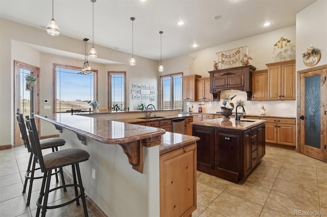 kitchen with sink, a breakfast bar, hanging light fixtures, kitchen peninsula, and a large island with sink