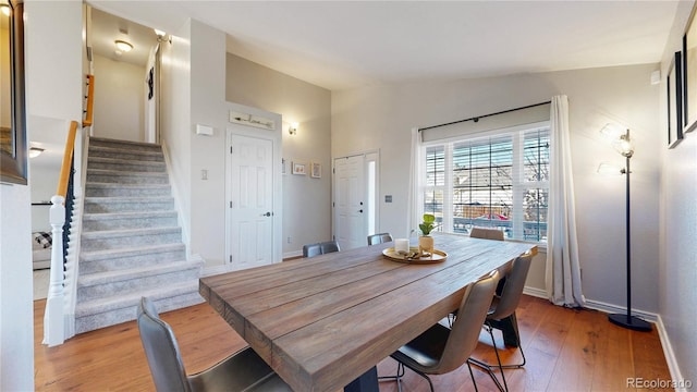 dining space with light wood-style floors, lofted ceiling, baseboards, and stairs