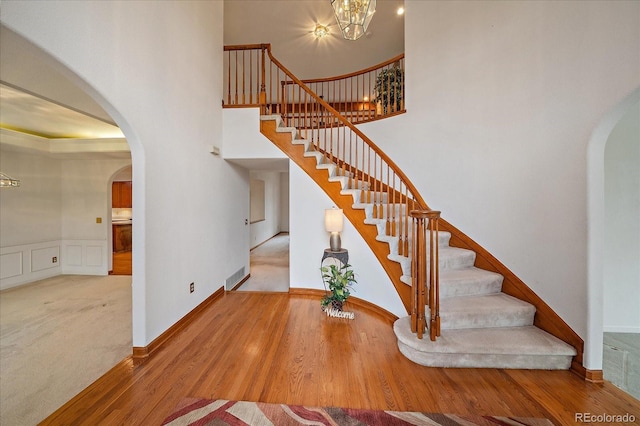 stairway featuring arched walkways, wood finished floors, a high ceiling, and a chandelier