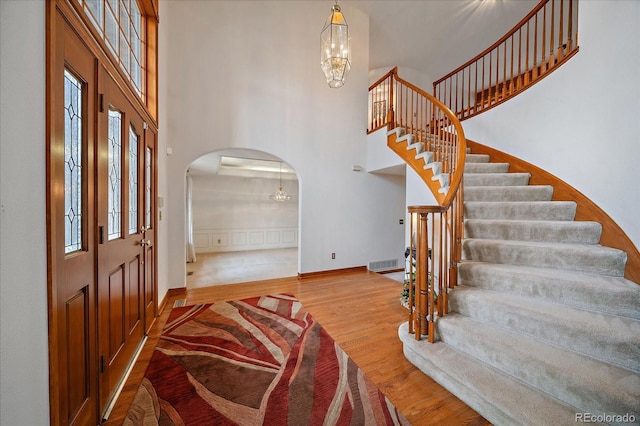 foyer entrance featuring a chandelier, arched walkways, a high ceiling, stairs, and wood finished floors