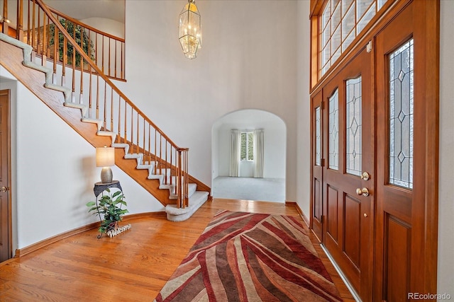 entrance foyer with stairs, wood finished floors, arched walkways, baseboards, and a towering ceiling