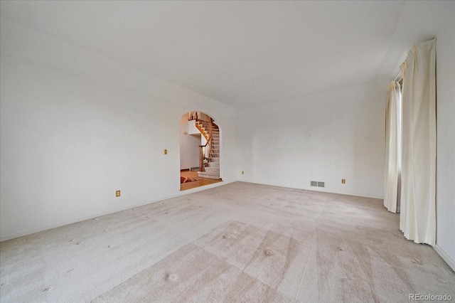 spare room featuring arched walkways, carpet, and stairway