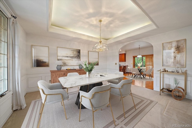 dining area featuring arched walkways, a tray ceiling, light carpet, a chandelier, and a decorative wall