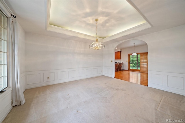 empty room with arched walkways, a tray ceiling, light colored carpet, a decorative wall, and a chandelier