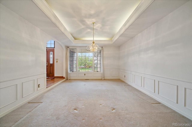 carpeted empty room featuring a decorative wall, a chandelier, a raised ceiling, and wainscoting