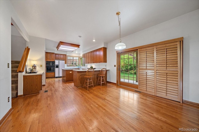 kitchen featuring white refrigerator with ice dispenser, black microwave, light wood-type flooring, brown cabinetry, and a peninsula