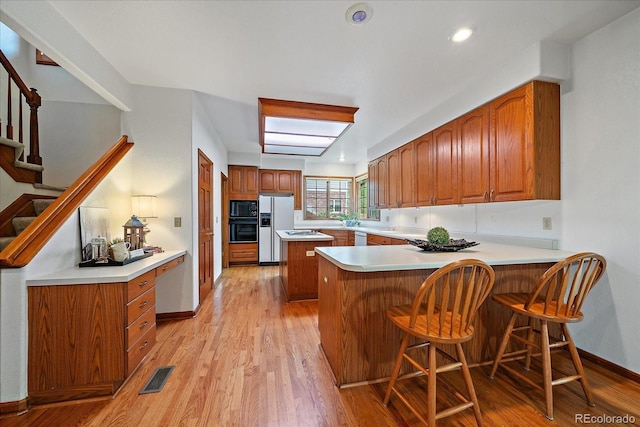 kitchen with black appliances, a peninsula, brown cabinets, light wood finished floors, and recessed lighting