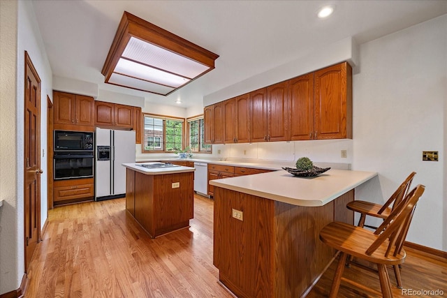 kitchen with black appliances, brown cabinetry, a peninsula, and light wood-style floors