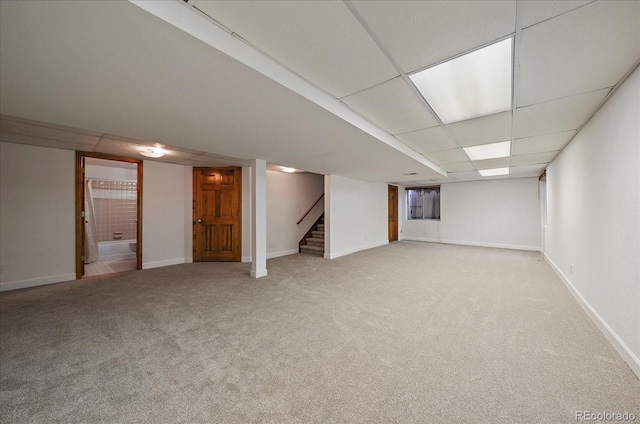finished basement with light colored carpet, stairway, a drop ceiling, and baseboards