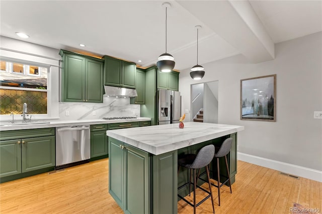 kitchen featuring light wood-style flooring, appliances with stainless steel finishes, under cabinet range hood, green cabinets, and a sink