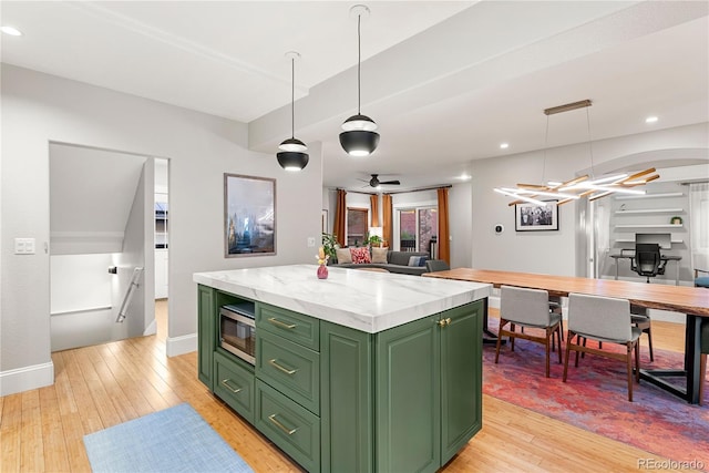 kitchen with decorative light fixtures, stainless steel microwave, light wood-style flooring, green cabinets, and a kitchen island