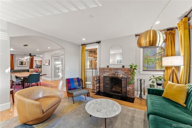 living area featuring light wood-style floors, plenty of natural light, a fireplace, and arched walkways