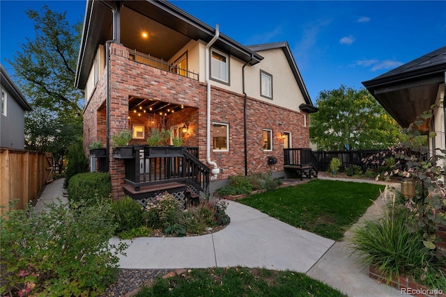 back of property featuring brick siding, fence, a balcony, and stucco siding