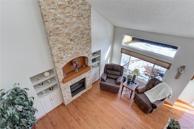 living room featuring high vaulted ceiling, light wood-type flooring, a textured ceiling, and a fireplace