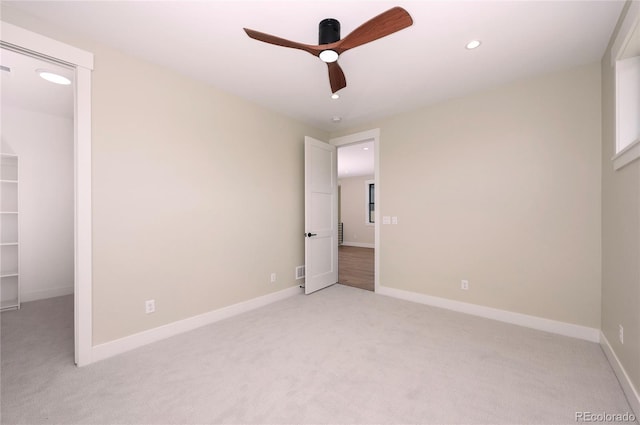 unfurnished bedroom featuring a spacious closet, light colored carpet, a closet, and ceiling fan