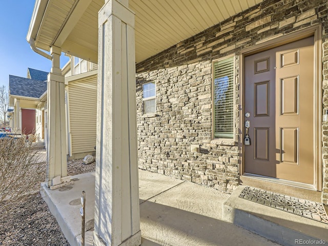 entrance to property featuring covered porch, brick siding, and a shingled roof