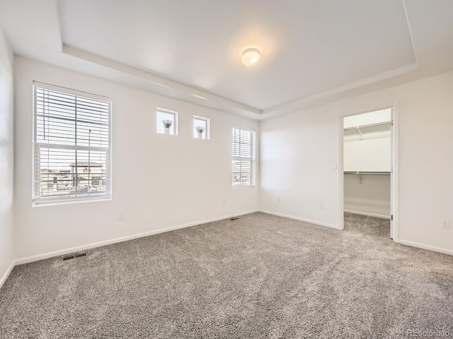 carpeted spare room featuring a raised ceiling, visible vents, and baseboards