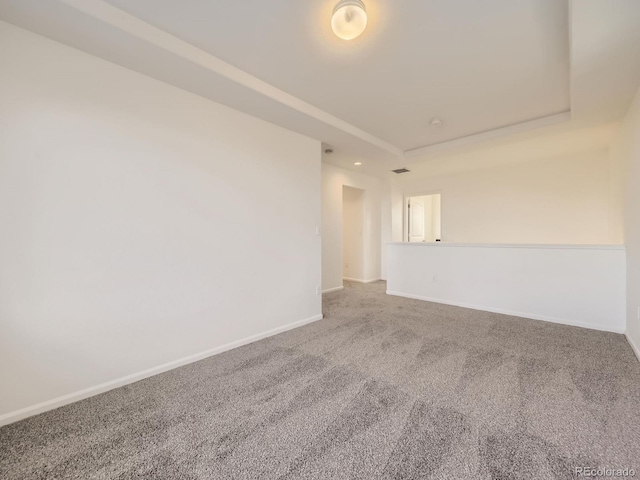 spare room with carpet floors, a tray ceiling, and baseboards