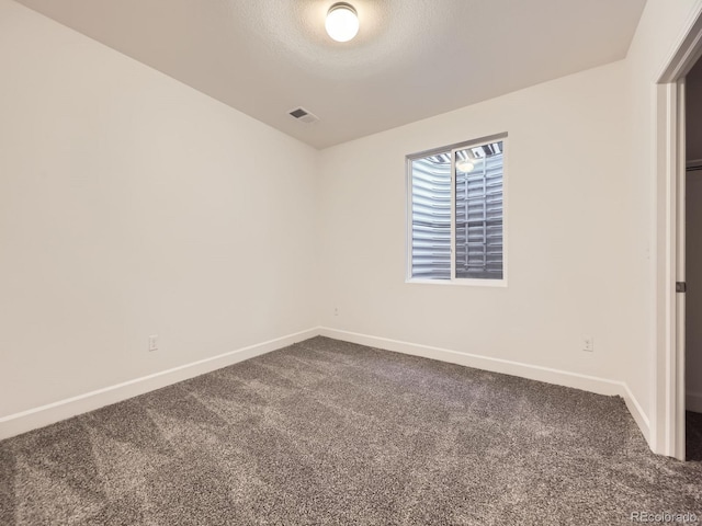 spare room featuring dark colored carpet, visible vents, a textured ceiling, and baseboards