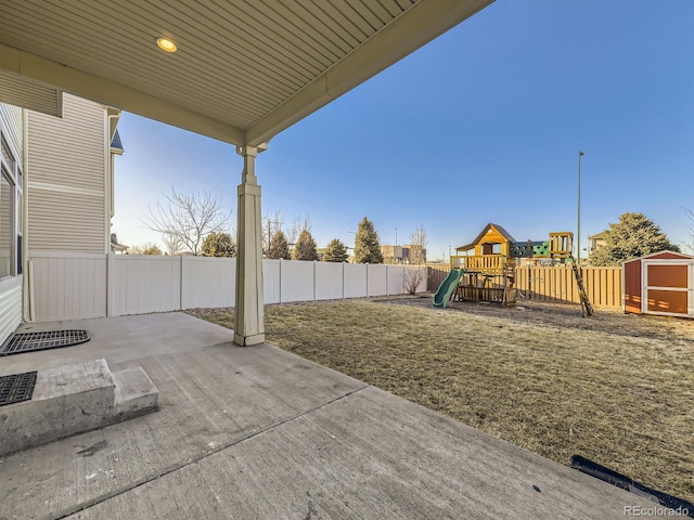 view of patio featuring an outbuilding, a fenced backyard, a playground, and a storage unit