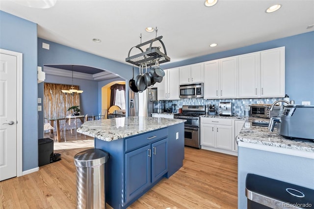 1929 Baguette Dr, Castle Rock, CO 80108 - kitchen featuring stainless steel appliances, arched walkways, blue cabinets, white cabinetry, and backsplash