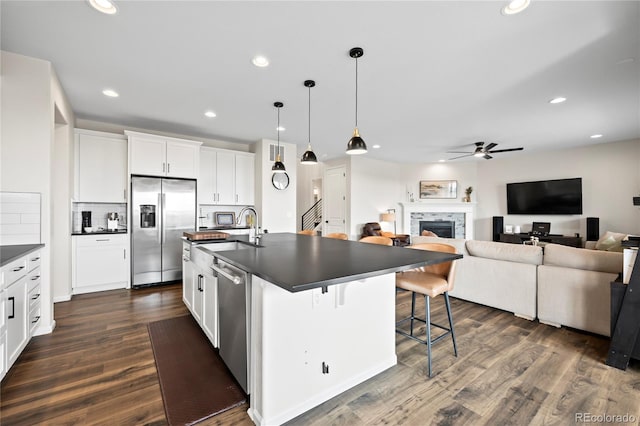 kitchen with dark countertops, an island with sink, a breakfast bar area, stainless steel appliances, and white cabinetry