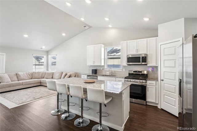 kitchen featuring a breakfast bar, stainless steel appliances, a center island, light stone counters, and white cabinets