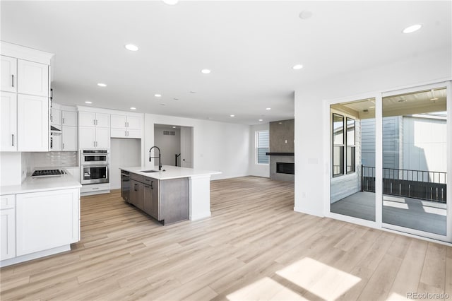 kitchen with light countertops, open floor plan, a kitchen island with sink, white cabinets, and a sink