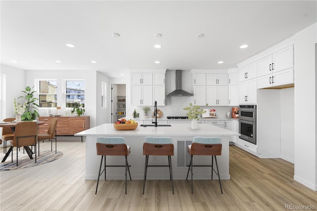 kitchen with a kitchen bar, light countertops, a sink, and wall chimney exhaust hood