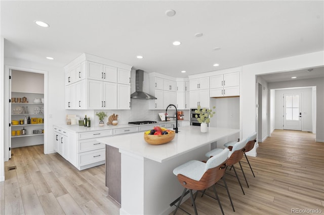 kitchen with a kitchen bar, light countertops, wall chimney exhaust hood, and white cabinetry