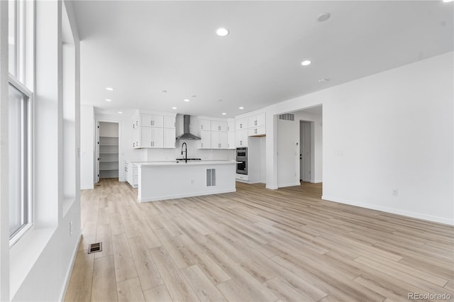 unfurnished living room featuring recessed lighting, visible vents, light wood-style flooring, a sink, and baseboards