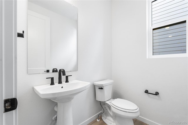 half bathroom featuring toilet, baseboards, and a sink