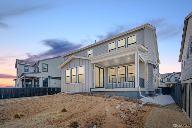 back of house at dusk featuring board and batten siding, fence, and central air condition unit