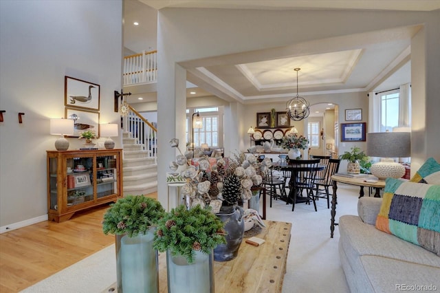 living area featuring a tray ceiling, stairway, wood finished floors, arched walkways, and ornamental molding