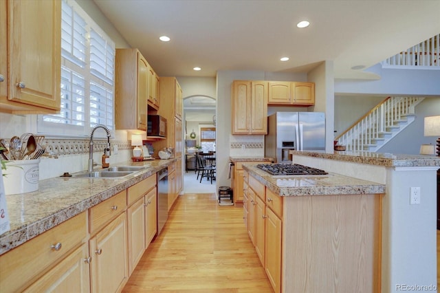 kitchen featuring stainless steel appliances, light brown cabinetry, a center island, a sink, and arched walkways