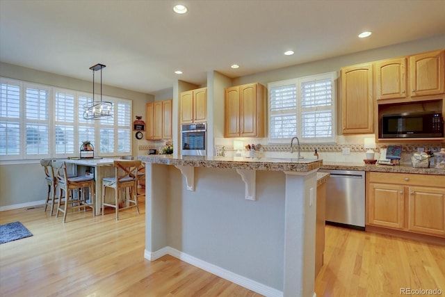 kitchen featuring light wood finished floors, a breakfast bar, light brown cabinetry, and stainless steel appliances