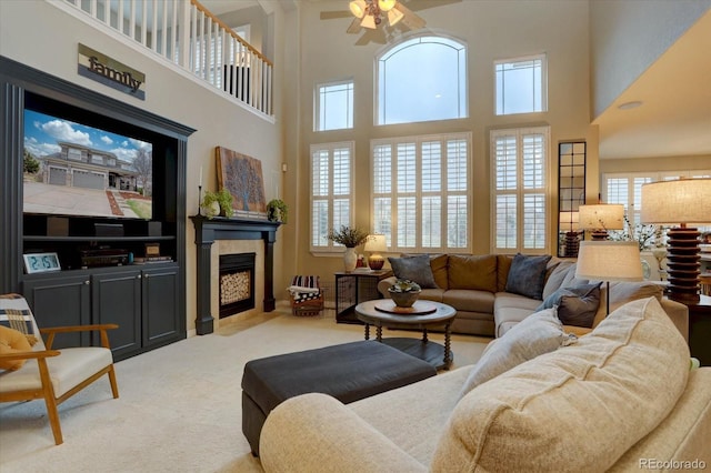 living area featuring carpet floors, a towering ceiling, a fireplace, and ceiling fan