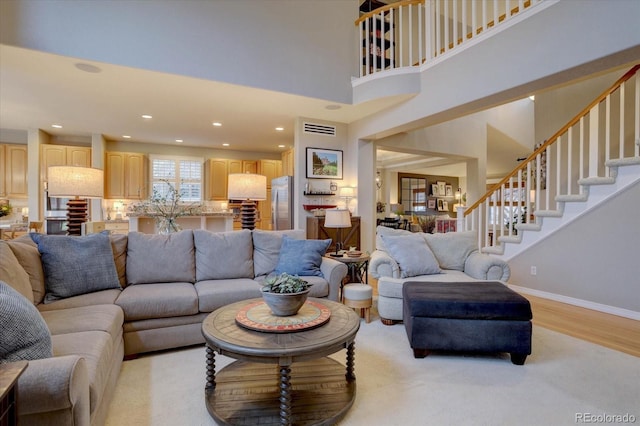 living room with stairs, recessed lighting, baseboards, a towering ceiling, and light wood-style floors