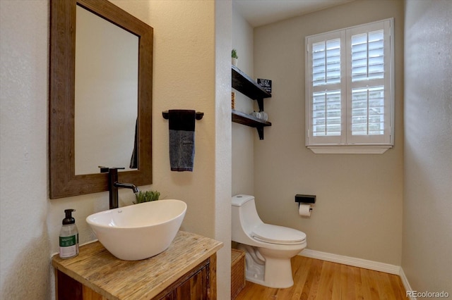 bathroom with toilet, wood finished floors, baseboards, and vanity