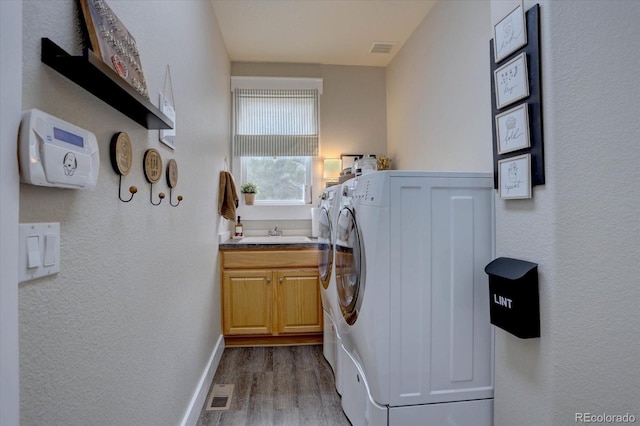 laundry room featuring a sink, separate washer and dryer, wood finished floors, visible vents, and cabinet space