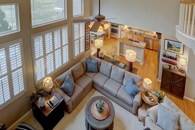 living room featuring baseboards, a high ceiling, light wood-style floors, and a ceiling fan
