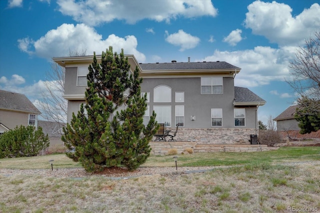 back of property featuring stone siding, stucco siding, central air condition unit, and a lawn
