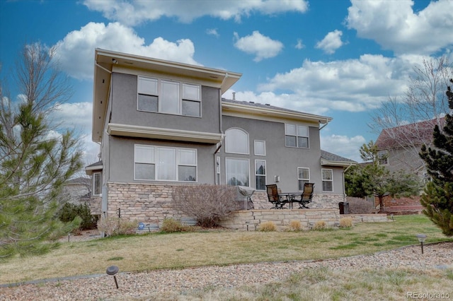 rear view of house featuring stone siding, a yard, and stucco siding