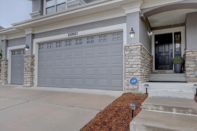 entrance to property with stone siding, concrete driveway, stucco siding, and an attached garage